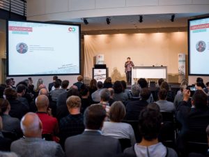 großer Saal mit Publikum und Bühne mit einer Person