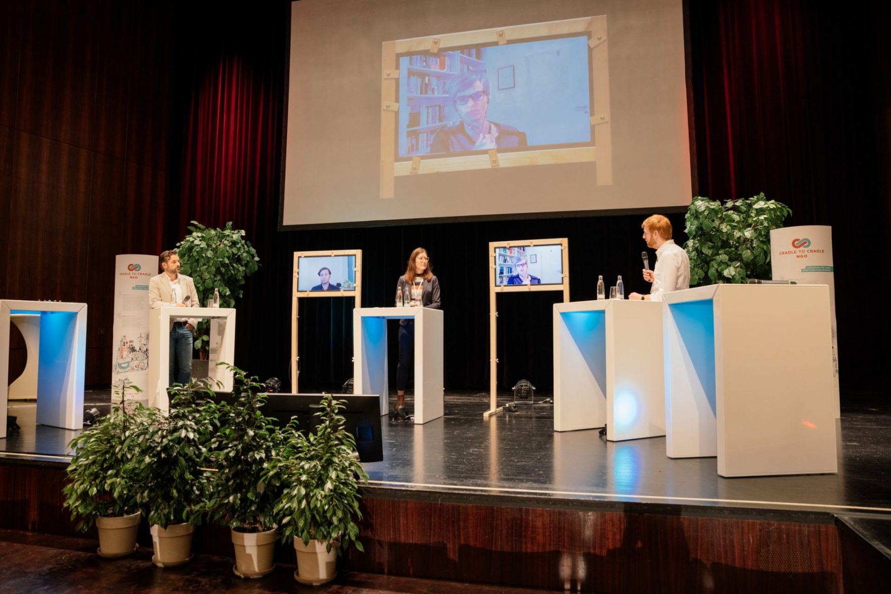 Speaker*innen auf der Bühne und Leinwand