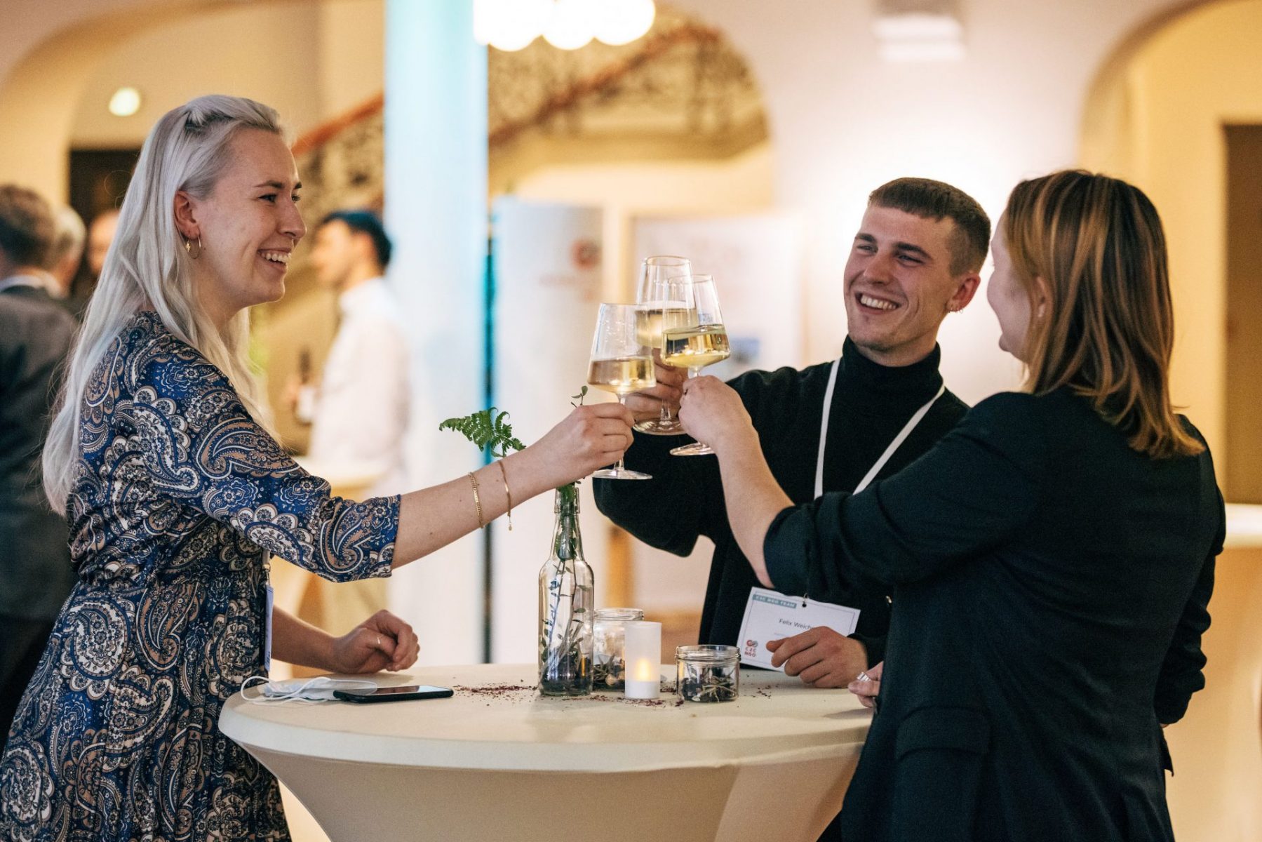 drei Personen stoßen mit Weingläsern an, lachen