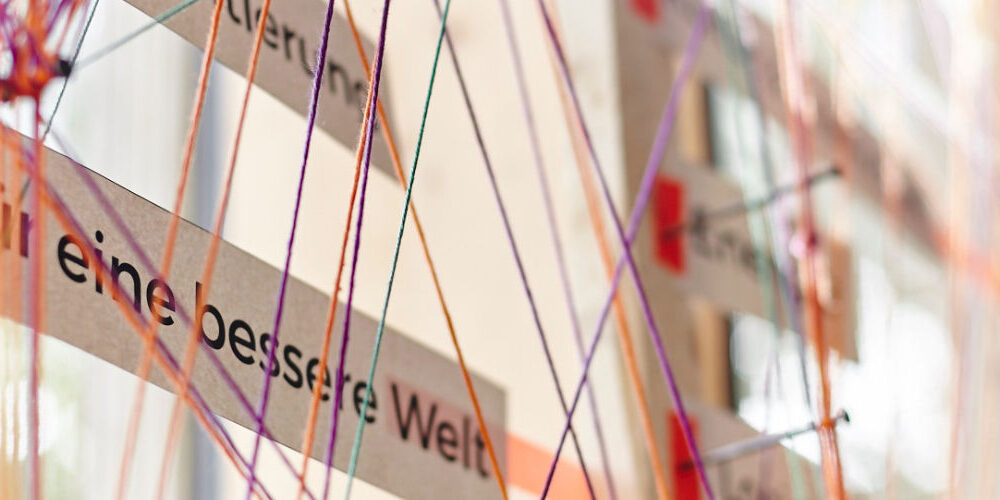 bunte Fäden laufen zusammen. für eine bessere Welt Schriftzug