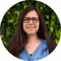 Isabel Gomez against green background, denim shirt, long brown hair, dark glasses, smiling