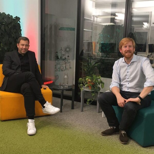 Tim Janßen, white man in shirt sitting, looks into camera. Next to it Lars Klingbeil, black suit, white man, white sneakers, sitting on yellow armchair