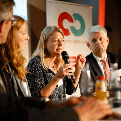 blonde white woman (Katja Hansen) sits on panel next to other people and speaks